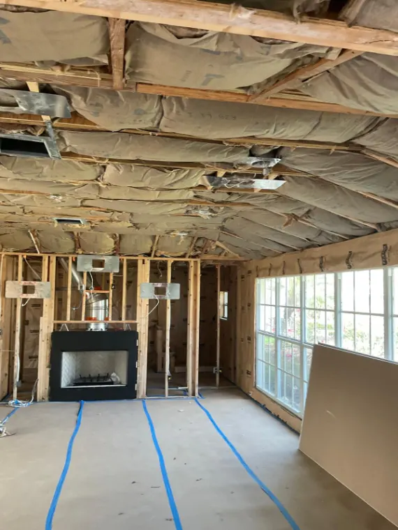 Living room opened to its framing and insulation, with the fireplace box in place